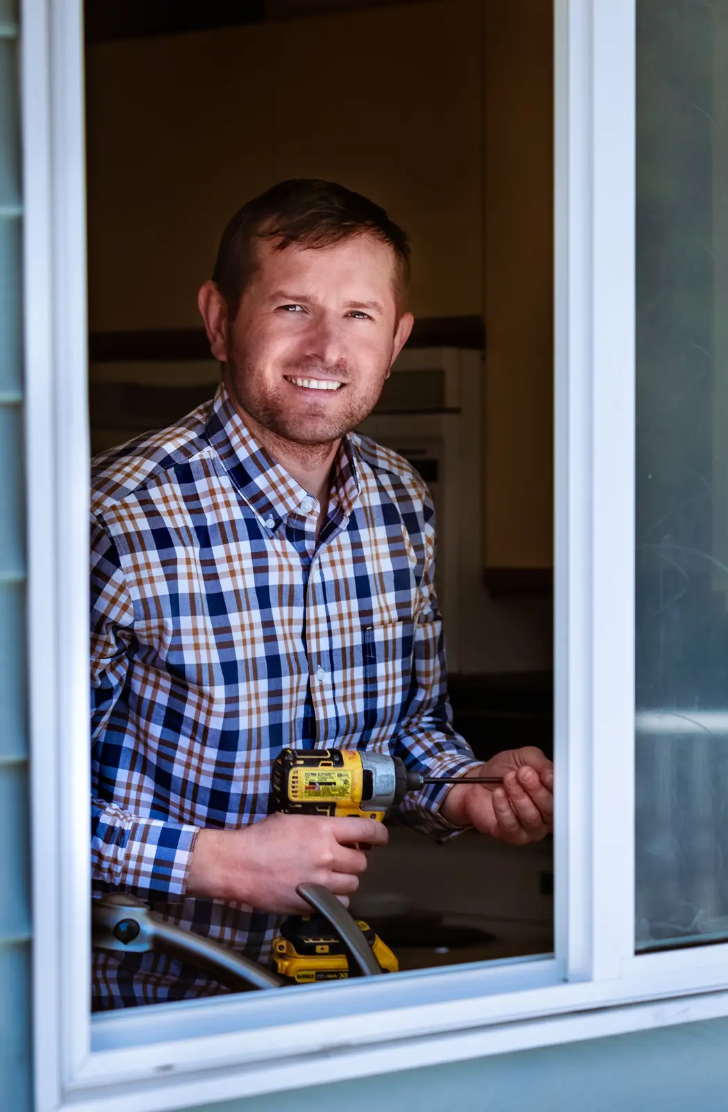 Smiling contractor holding a cordless drill at an open window of a home Digital marketing agency: smiling contractor holding a cordless drill at an open window of a home