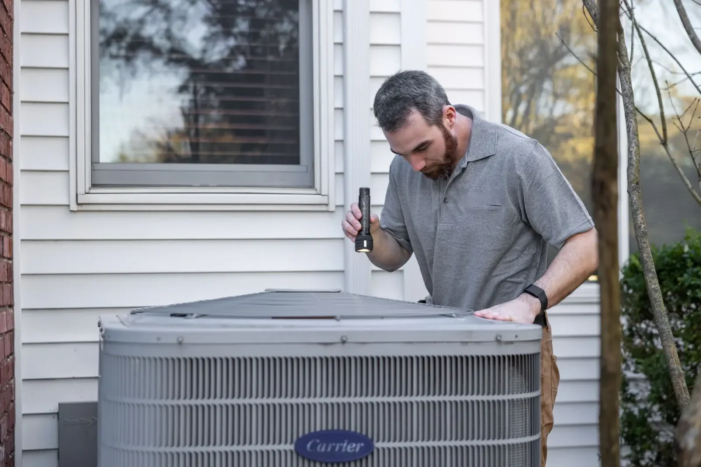 HVAC technician inspecting an outdoor air conditioning unit beside a home HVAC marketing: HVAC technician inspecting an outdoor air conditioning unit beside a home
