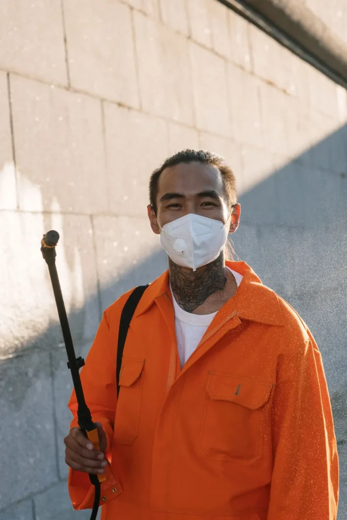 Local SEO Charleston: pest control technician in orange coveralls and a face mask holding a sprayer wand